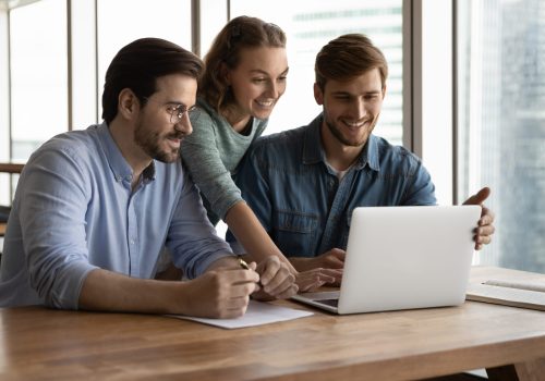 Happy,Three,Teammates,Working,Together,On,Online,Project,,Sitting,At we